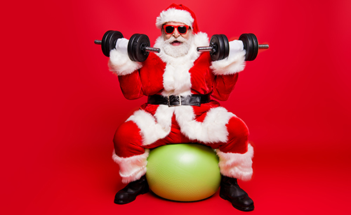 Cheerful sporty muscular virile strong Santa in white fluffy gloves fur coat sitting on pilates ball work out ready for sale promo discount wishing merry x mas isolated on red background fun joy