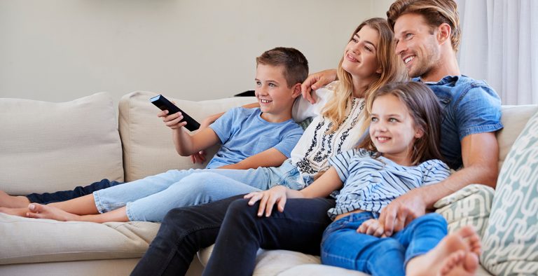 Family Sitting On Sofa At Home Watching TV Together